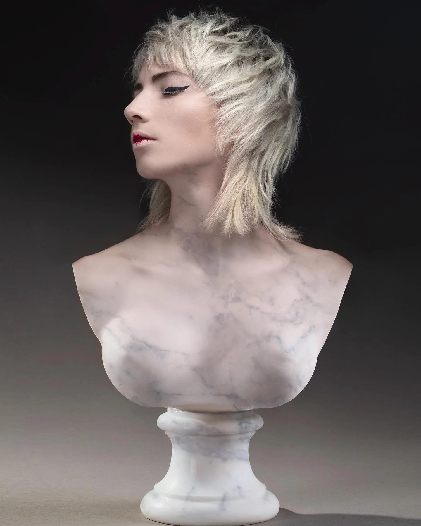 Coupe shag blond platine texturée, de profil, sur un buste de marbre